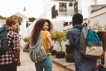 Rear view of teenage friends walking together in the street. Smiling teenage girl walking with friends wearing college bag. - JLPSF11441