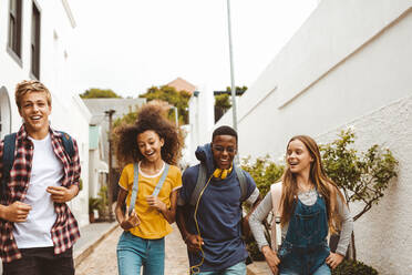 Eine Gruppe multiethnischer Jugendlicher genießt einen Spaziergang auf der Straße. Fröhliche College-Freunde gehen mit Rucksäcken durch eine Gasse. - JLPSF11442
