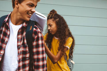 Nahaufnahme von Freunden im Teenageralter, die im Freien stehen und College-Taschen tragen. Ein Mädchen schreibt in ein Buch und hält es zur Unterstützung auf dem Rücken ihrer Freundin. - JLPSF11451