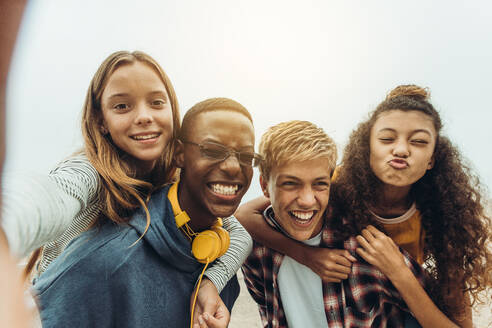 Nahaufnahme von vier glücklichen Teenager-Freunden, die ein Selfie im Freien machen. Die Mädchen reiten Huckepack auf den Jungen, während sie ein Selfie im Freien machen. - JLPSF11452