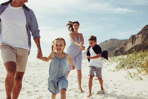 Glückliche Familie im Urlaub, die zusammen am Strand läuft. Kinder haben Spaß mit den Eltern im Strandurlaub. - JLPSF11461