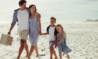 Kids walking with their parent along the beach on summer day. Family of four at beach for a picnic. - JLPSF11463