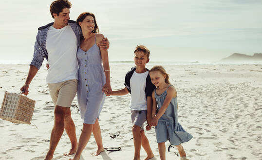 Kinder, die an einem Sommertag mit ihren Eltern am Strand spazieren gehen. Vierköpfige Familie am Strand bei einem Picknick. - JLPSF11463