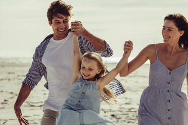 Ein Paar, das seine Tochter an der Hand hält und am Strand spielt, ein Mädchen, das sich mit seinen Eltern im Urlaub amüsiert. - JLPSF11464