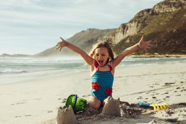 Cute girl playing on the beach making a castle. Beautiful girl building a sandcastle on seaside on summer vacation. - JLPSF11471