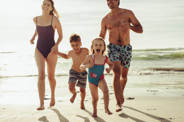 Aufgeregtes Mädchen, das mit seiner Familie am Strand läuft. Vierköpfige Familie, die sich im Sommerurlaub amüsiert. - JLPSF11472