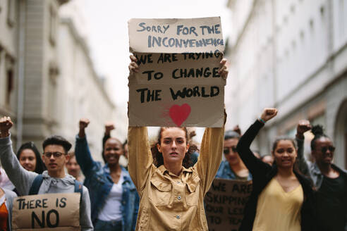 Junge Studentin hält Plakat und protestiert. Gruppe von Demonstranten, die gegen den Klimawandel protestieren. - JLPSF11497