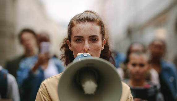 Weibliche Aktivistin protestiert mit Megaphon während eines Streiks mit einer Gruppe von Demonstranten im Hintergrund. Eine Frau protestiert in der Stadt. - JLPSF11513