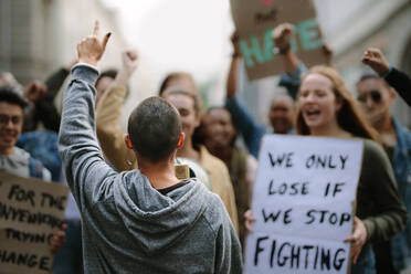 Eine weibliche Aktivistin, die bei einem Protestmarsch in ein Megaphon schreit. Jugendliche protestieren mit Plakaten und Megaphon. - JLPSF11519