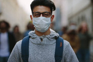 Young man wearing a face mask participate in a protest with group of demonstrator in background. Man protesting with group of rebellions outdoors on road. - JLPSF11528