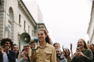 Junge Frau mit einer Gruppe von Menschen bei einer Kundgebung. Frau mit einem Megaphon im Freien auf der Straße während einer Demonstration. - JLPSF11571
