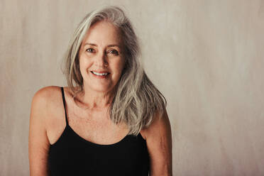 Closeup shot of an aging woman smiling while posing in her natural body. Body positive woman in black underwear embracing her body. Woman standing alone against a studio background. - JLPSF11588