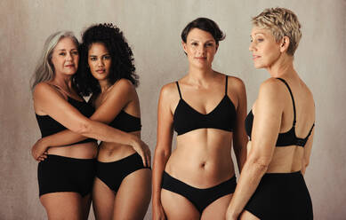 Models unterschiedlichen Alters, die ihren natürlichen und alternden Körper zelebrieren. Vier körperbewusste und selbstbewusste Frauen, die schwarze Unterwäsche tragen und zusammen in einem Studio stehen. - JLPSF11592