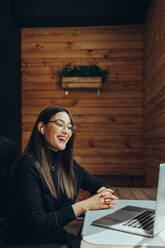 Businesswoman smiling happily during an online meeting in a modern co-working space. Cheerful female entrepreneur communicating with her business associates while working remotely. - JLPSF11608