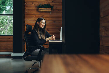 Junge Geschäftsfrau, die während eines Online-Meetings in einem modernen Co-Working Space fröhlich lächelt. Fröhliche Unternehmerin, die mit ihren Geschäftspartnern kommuniziert, während sie aus der Ferne arbeitet. - JLPSF11609