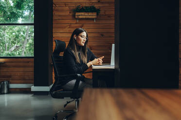 Eine Geschäftsfrau bei einer virtuellen Besprechung in einem modernen Co-Working Space. Eine junge Unternehmerin kommuniziert mit ihren Geschäftspartnern, während sie aus der Ferne arbeitet. - JLPSF11610