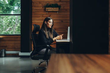 Female business professional having a virtual meeting in a modern co-working space. Young female entrepreneur communicating with her business associates while working remotely. - JLPSF11610