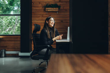 Lächelnde Unternehmerin bei einem virtuellen Meeting in einem modernen Co-Working Space. Glückliche junge Geschäftsfrau, die mit ihren Geschäftspartnern kommuniziert, während sie aus der Ferne arbeitet. - JLPSF11611