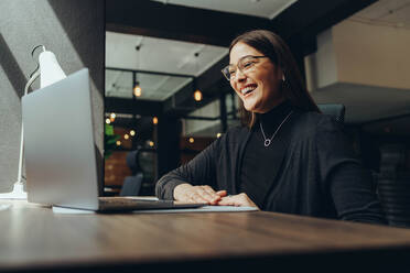 Lächelnde Geschäftsfrau, die an einem Online-Meeting in einem modernen Co-Working-Büro teilnimmt. Glückliche Unternehmerin, die mit ihren Geschäftspartnern kommuniziert, während sie aus der Ferne arbeitet. - JLPSF11612