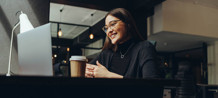 Erfolgreiche Geschäftsfrau, die während eines Online-Meetings in einem modernen Co-Working-Büro fröhlich lächelt. Glückliche Unternehmerin, die mit ihren Geschäftspartnern kommuniziert, während sie aus der Ferne arbeitet. - JLPSF11614