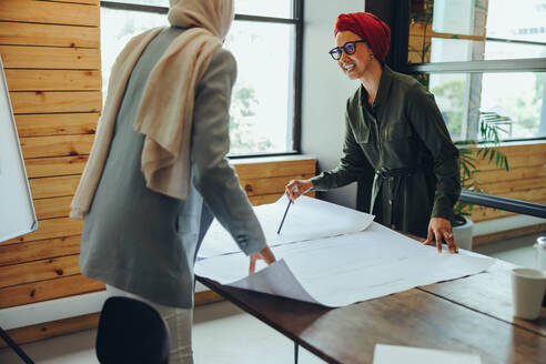 Zwei muslimische Designer diskutieren bei der Arbeit mit Plänen. Kreative Geschäftsfrauen planen ein innovatives Projekt. Architektinnen mit Kopftüchern an einem integrativen Arbeitsplatz. - JLPSF11674