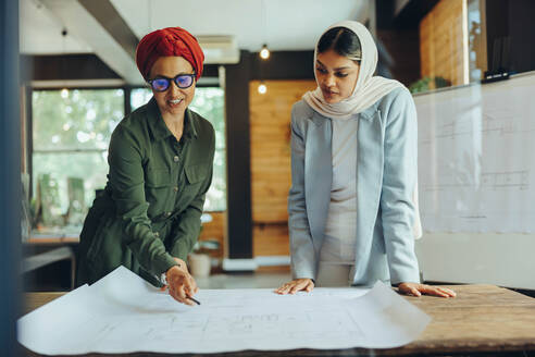 Muslimische Architekten, die in einem modernen Büro an Entwürfen arbeiten. Zwei kreative Geschäftsfrauen, die ein neues innovatives Projekt planen. Designerinnen mit Kopftüchern an einem integrativen Arbeitsplatz. - JLPSF11676