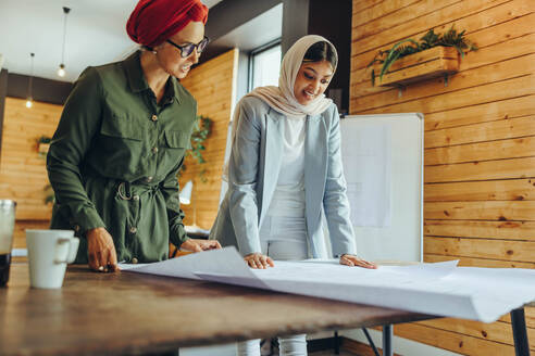 Kreative Architektinnen, die in einem modernen Büro an Entwürfen arbeiten. Zwei muslimische Geschäftsfrauen, die ein neues innovatives Projekt planen. Zwei Designerinnen mit Kopftuch an einem integrativen Arbeitsplatz. - JLPSF11680