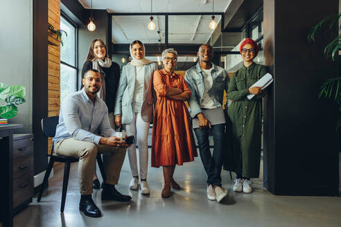 Ein Team unterschiedlicher Geschäftsleute lächelt in einem modernen Büro in die Kamera. Eine Gruppe multikultureller Unternehmer, die ein erfolgreiches Start-up in einem integrativen Arbeitsumfeld betreiben. - JLPSF11710