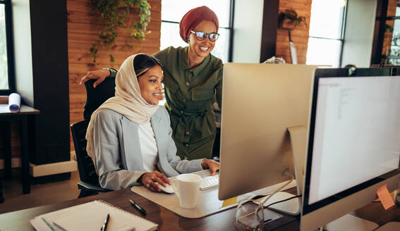Zwei muslimische Geschäftsfrauen diskutieren in einem Büro vor einem Computerbildschirm. Fröhliche Geschäftsfrauen arbeiten als Team in einem modernen Co-Working-Büro. - JLPSF11728