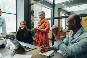 Verschiedene Geschäftsleute, die während einer Besprechung in einem modernen Büro fröhlich lächeln. Gruppe erfolgreicher Geschäftsleute, die an einem multikulturellen Arbeitsplatz als Team arbeiten. - JLPSF11757