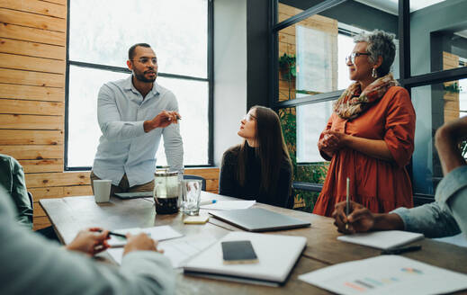 Eine Gruppe verschiedener Geschäftsleute tauscht während einer Besprechung in einem modernen Büro strategische Ideen aus. Ein Team von multikulturellen Geschäftsleuten arbeitet an einem kreativen Arbeitsplatz zusammen. - JLPSF11759