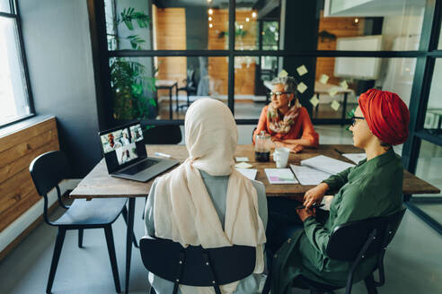 Ethnische Geschäftsfrauen, die an einer virtuellen Sitzung in einem modernen Büro teilnehmen. Multikulturelle Geschäftsfrauen, die eine Videokonferenz mit ihren Geschäftspartnern an einem kreativen Arbeitsplatz abhalten. - JLPSF11761