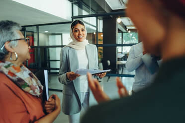 Muslimische Geschäftsfrau, die in einem modernen Büro den Applaus ihrer Kollegen entgegennimmt. Erfolgreiche Geschäftsfrau, die eine Sitzung in einem multikulturellen Arbeitsumfeld leitet. - JLPSF11817