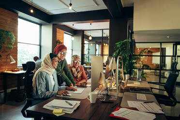 Multicultural businesswomen working as a team in a modern co-working office. Group of happy businesswomen smiling cheerfully while looking at a computer screen in an inclusive workplace. - JLPSF11825