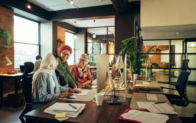 Glückliche Geschäftsfrauen, die in einem modernen Co-Working-Büro zusammenarbeiten. Eine Gruppe multikultureller Geschäftsfrauen lächelt fröhlich, während sie an einem integrativen Arbeitsplatz eine Diskussion führen. - JLPSF11826