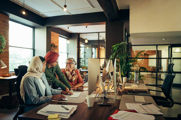 Fröhliche Geschäftsfrauen, die als Team in einem modernen Co-Working-Büro arbeiten. Eine Gruppe multikultureller Geschäftsfrauen lächelt fröhlich, während sie an einem integrativen Arbeitsplatz eine Diskussion führen. - JLPSF11827