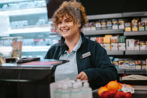 Frau, die als Kassiererin in einem Supermarkt arbeitet und den Kunden anlächelt. - JLPSF11840