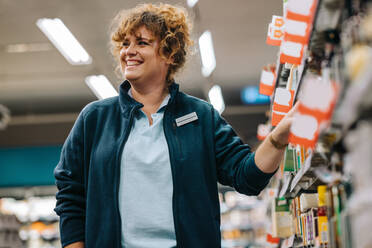 Female worker working in store. Grocery store manager standing in aisle and smiling. - JLPSF11849