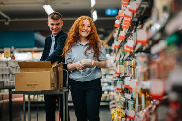 Zwei junge Angestellte in einem Supermarkt. Ein Mann und eine Frau, die im Supermarkt arbeiten und die Regale auffüllen. - JLPSF11854