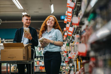 Man and woman working at a supermarket restocking the shelves. Two employees working together in grocery store. - JLPSF11855
