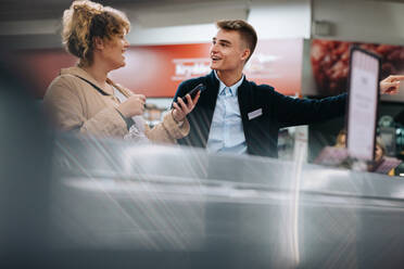 Friendly grocery store worker assisting female customer. Young employee helping shopper at the supermarket. - JLPSF11865