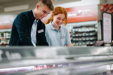 Männliche und weibliche Angestellte arbeiten zusammen in einem Supermarkt. Auszubildende füllen Produkte in einem Lebensmittelladen auf. - JLPSF11867