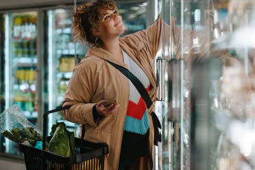 Frau, die im Supermarkt Lebensmittel aus einem Kühlregal holt. Weibliche Einkäuferin im Lebensmittelgeschäft, die Lebensmittel kauft. - JLPSF11871