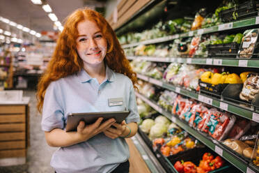 Nahaufnahme eines jungen Arbeiters mit digitalem Tablet in einem Lebensmittelgeschäft. Zufriedener Auszubildender im Supermarkt. - JLPSF11879