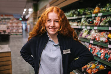 Porträt einer Frau, die in einem Supermarktgang steht, in die Kamera schaut und lächelt. Frau arbeitet in einem Lebensmittelgeschäft. - JLPSF11882