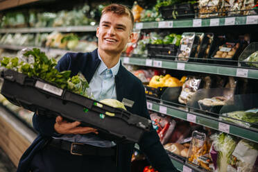 Ein Mann arbeitet in einem Supermarkt und füllt frisches Obst und Gemüse in der Gemüseabteilung auf. Ein junger Arbeiter arbeitet im Supermarkt. - JLPSF11884