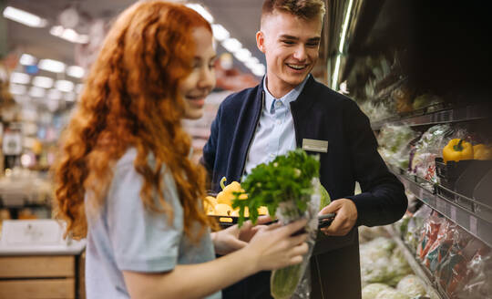 Supermarktangestellte, die frische Produkte in die Regale einpacken. Angestellte eines Lebensmittelgeschäfts, die in der Gemüseabteilung arbeiten. - JLPSF11886