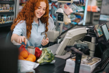 Woman cashier scanning grocery items at checkout counter. Woman working at billing counter in grocery store. - JLPSF11890