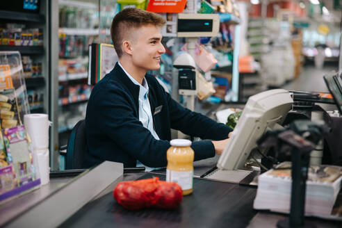 Ein Mann arbeitet an der Kasse eines Supermarktes, ein junger Angestellter bei einem Ferienjob im Supermarkt. - JLPSF11893