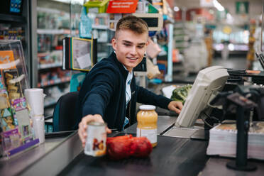 Man serving customers at supermarket checkout. Male sales clerk scanning products at grocery store checkout. - JLPSF11894